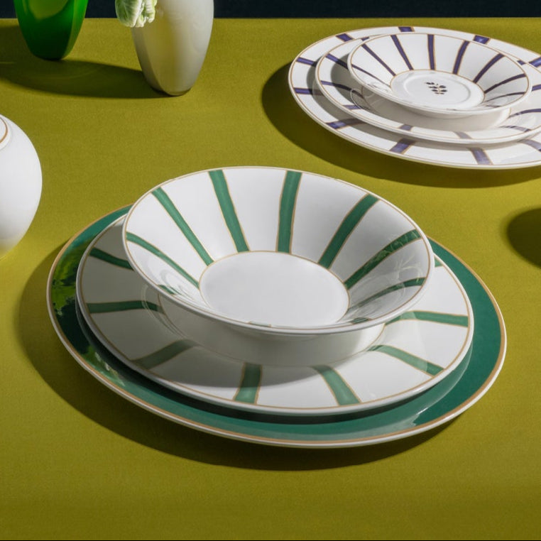 Collection of ceramic tableware including plates, cups, and a teapot on a green surface with a dark background.