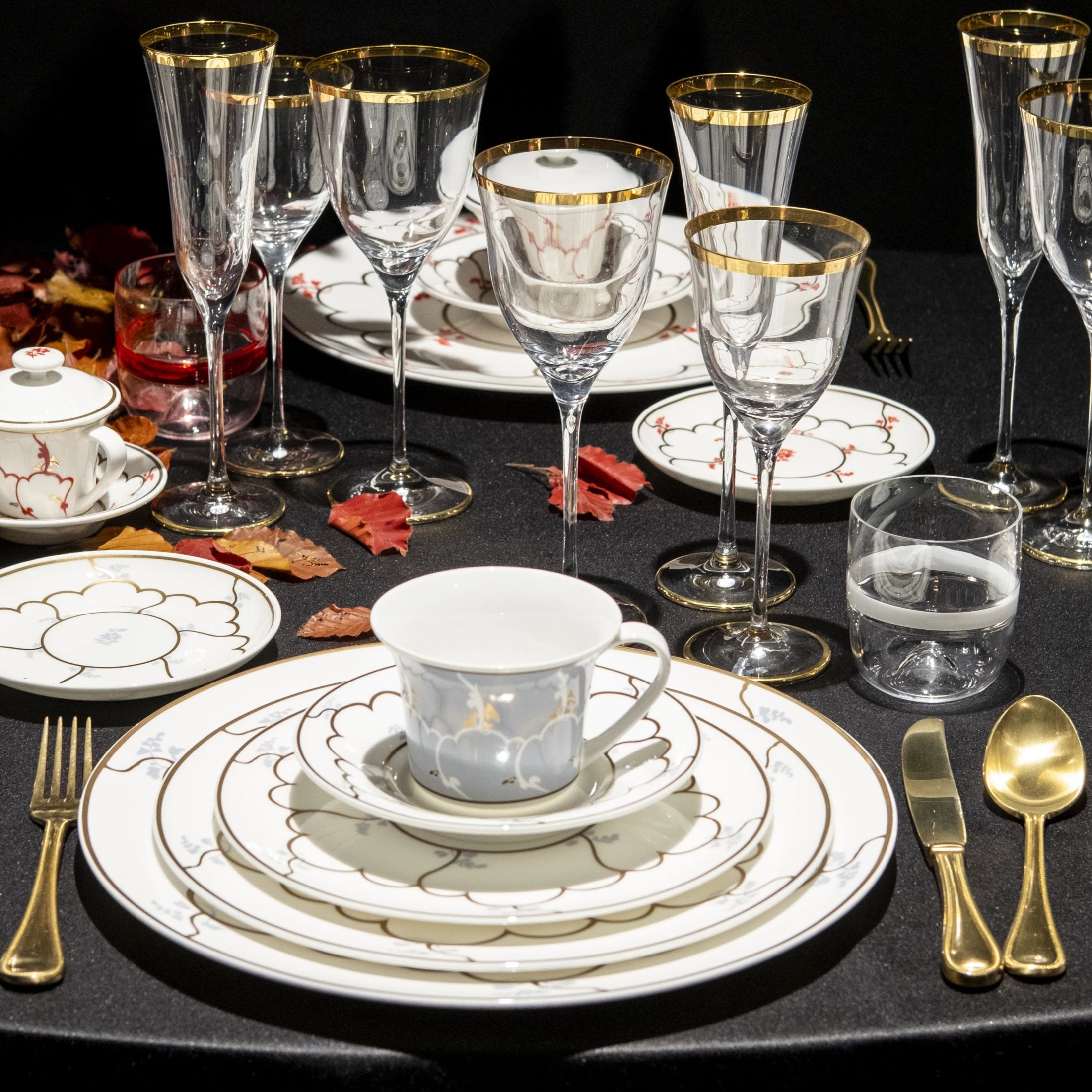Dining table set with elegant dinnerware, glasses, and cutlery on a black surface.