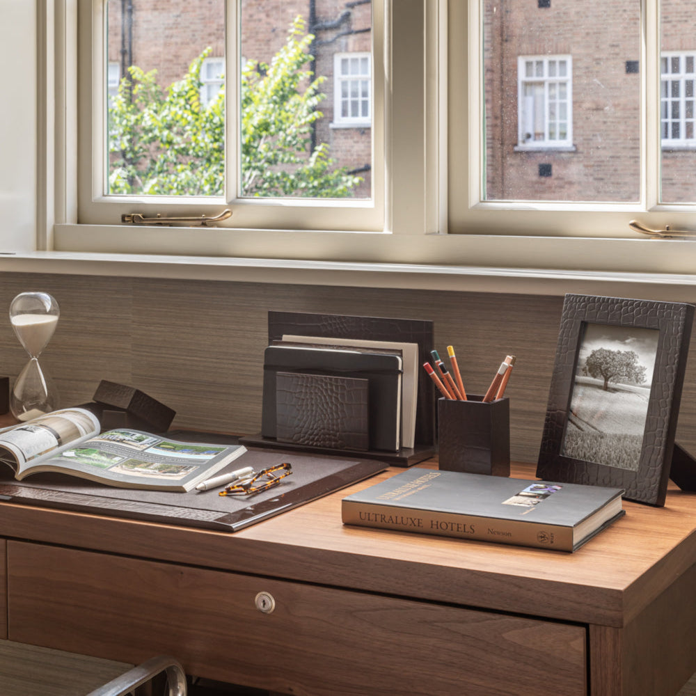 Wooden desk with office supplies in a room with large windows.