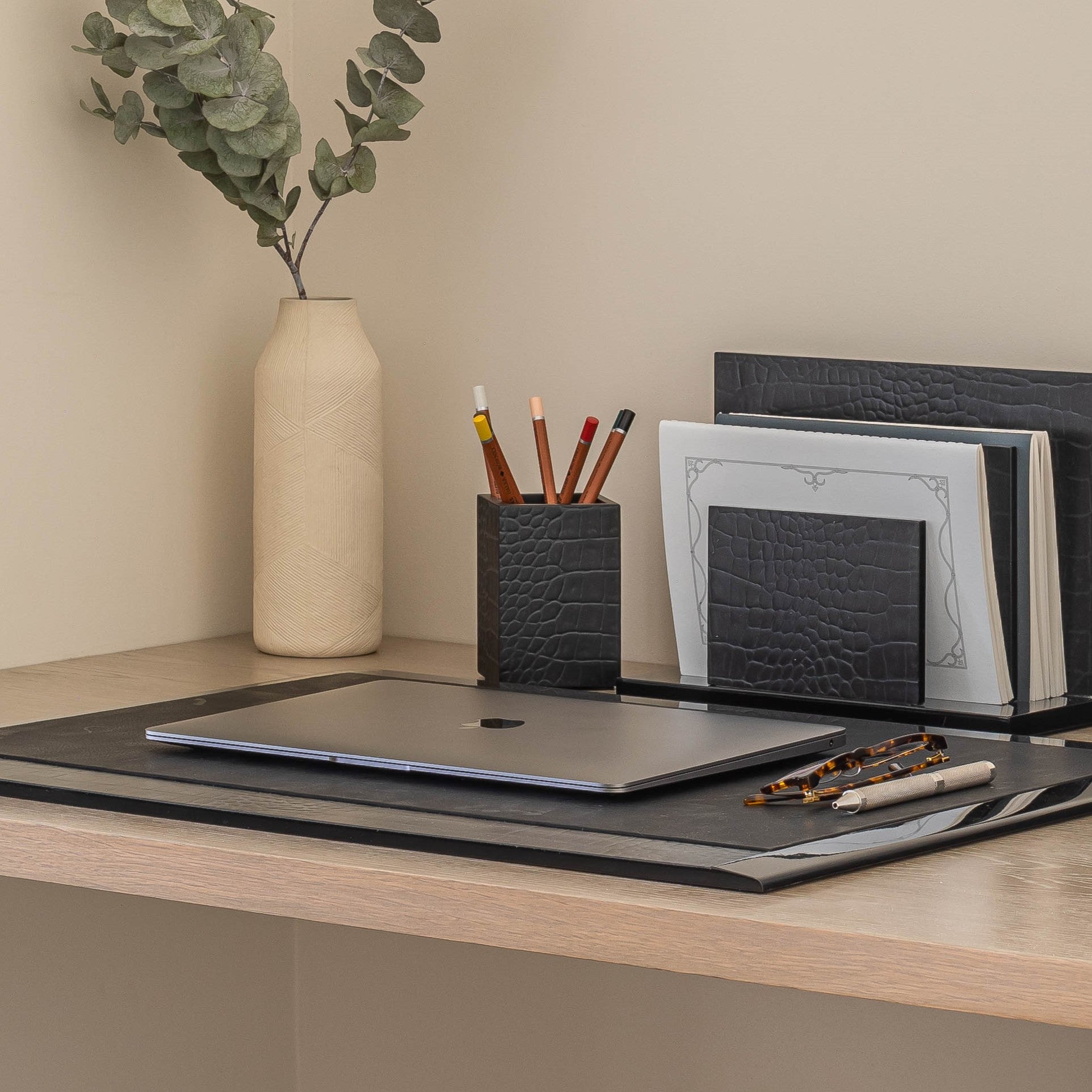 Desk setup with laptop, stationery items, and a vase on a neutral background
