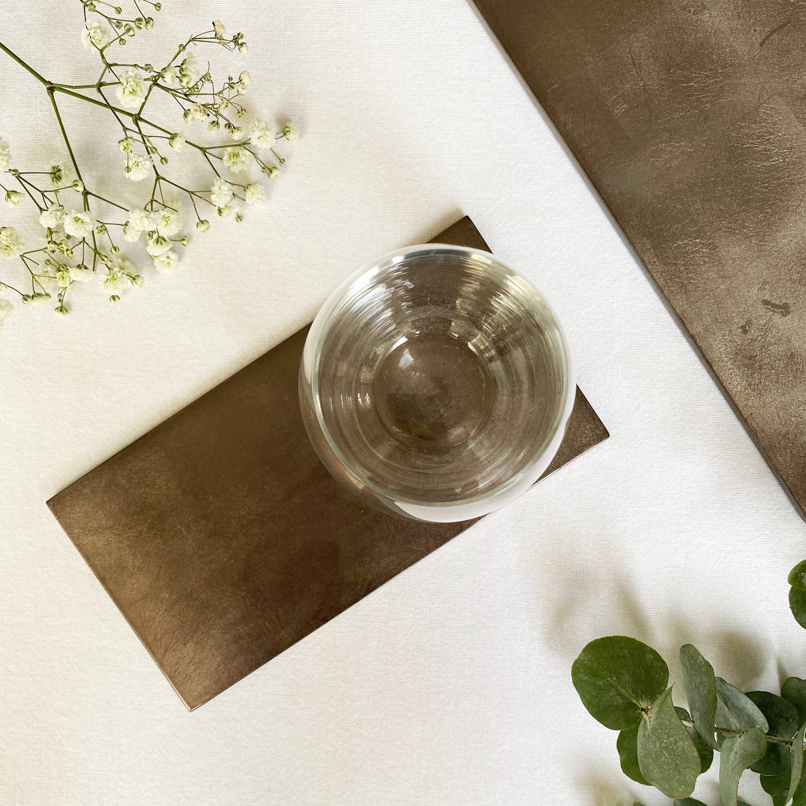 Clear glass bowl on a brown rectangular mat with white flowers and green leaves on a light surface