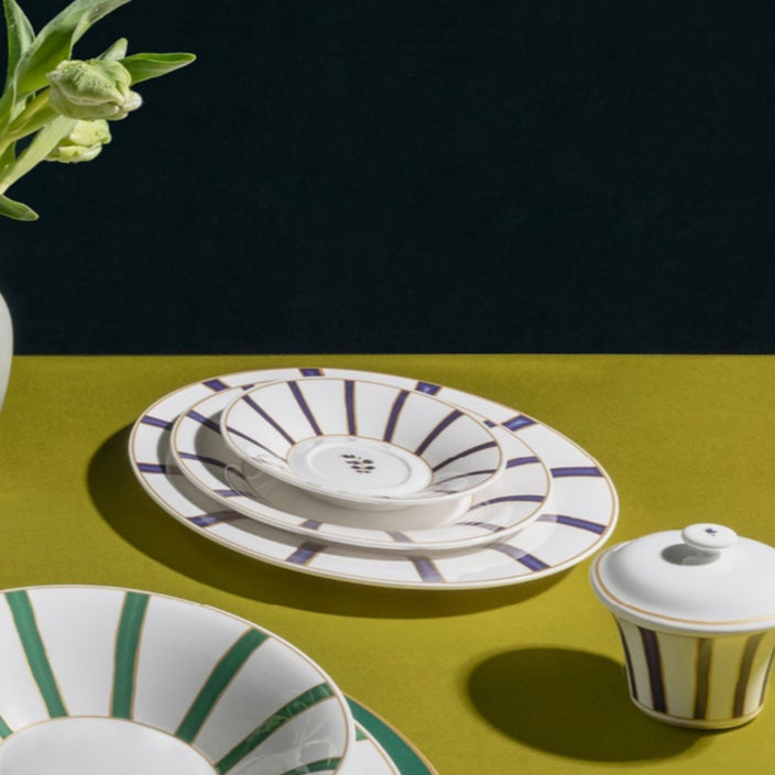 Collection of ceramic tableware including plates, cups, and a teapot on a green surface with a dark background.