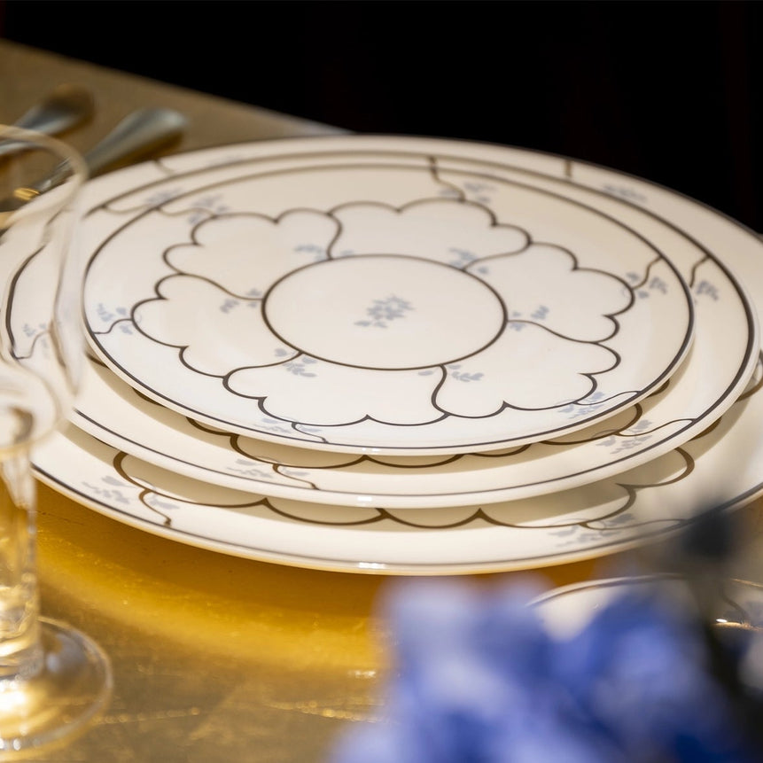 Set of decorative plates with floral patterns on a table with glasses and cutlery.