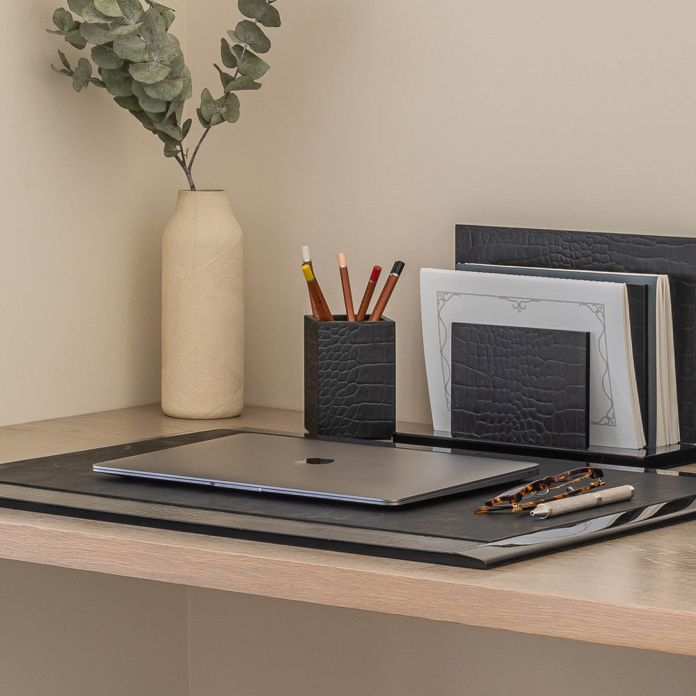 Desk setup with laptop, stationery items, and a vase on a neutral background