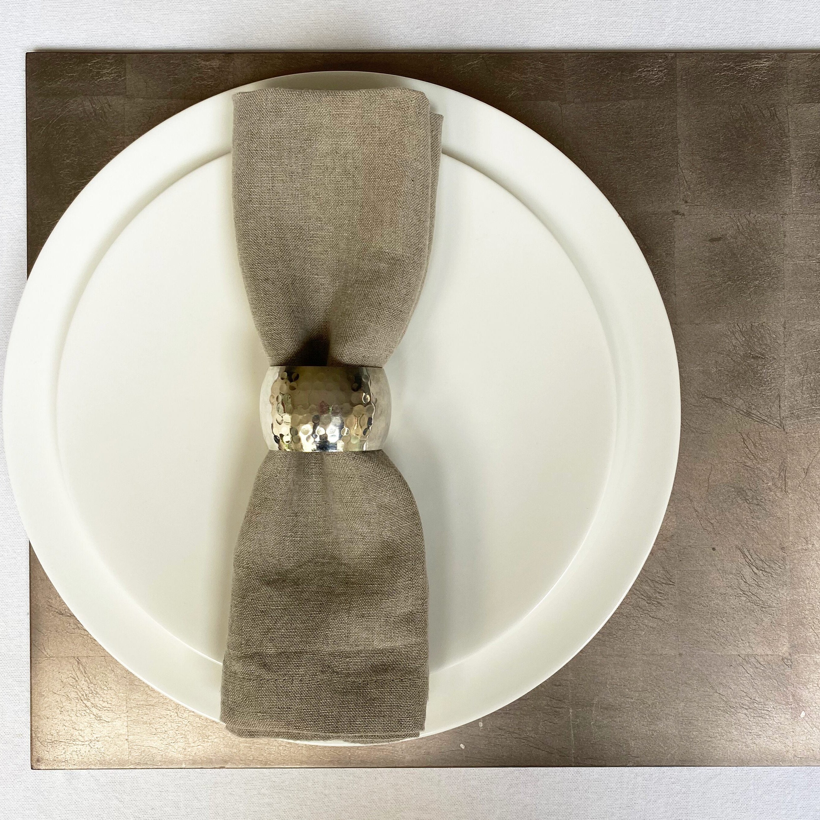 White plate with a folded gray napkin on a metallic surface